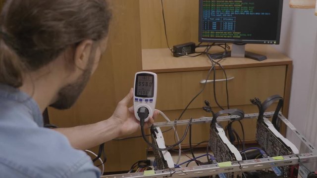 Expert technician using a power meter monitoring and indicating consumption and cost of gpu cryptocurrency mining rig