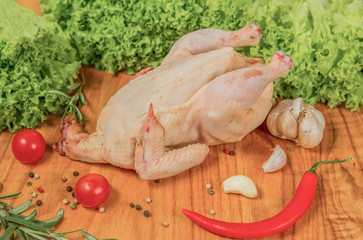 Fresh chicken on a cutting board with cherry tomatoes, lettuce, garlic, chilli, rosemary, onion