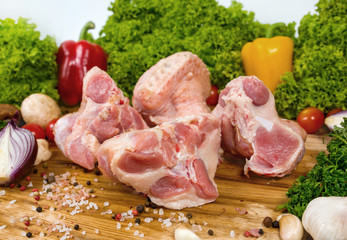 Raw meat, turkey meat on a cutting wooden board with cherry tomatoes, lettuce leaves, garlic, chilli pepper, rosemary, onion