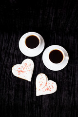 on a black background are two cups of coffee and biscuits in the form of heart