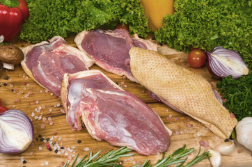 Four fillets of turkey with a skin on a cutting wooden board with cherry tomatoes, lettuce, garlic, chilli, rosemary, onion. Preparation of a festive dinner