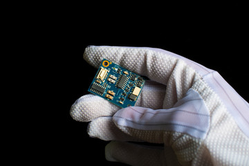 hand in white glove holding a microcircuit. Black background