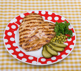 Fried chicken, recently cooked on charcoal. Fillet of cooked chicken, served on a plate with peas, cucumbers and parsley