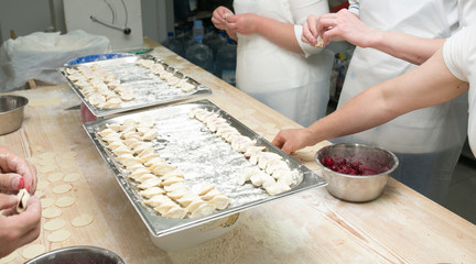 Dumplings in flour on a board for cooking, ready-made dumplings in two large trays, four chefs prepare a dumpling in the kitchen of the restaurant