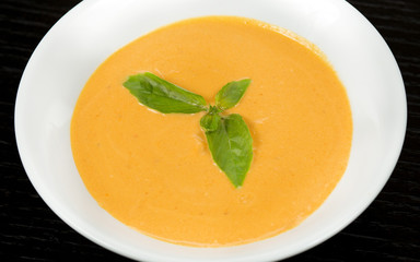 Pumpkin and carrot soup with cream and parsley on a dark wooden background