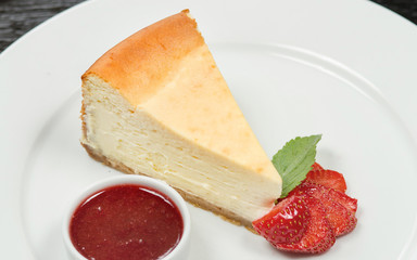 Piece of cheesecake on a white plate, decorated with fresh strawberry slices and piracotta with strawberry jam