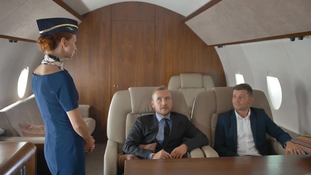 Entrepreneurs in private jet relaxing while flying and speaking with stewardess