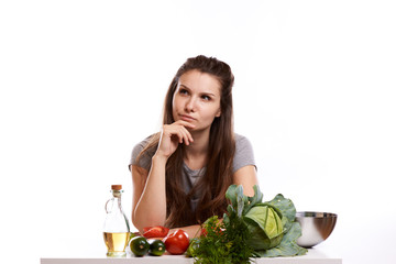 happy adult woman with various fresh vegetables on kitchen table looking at camera