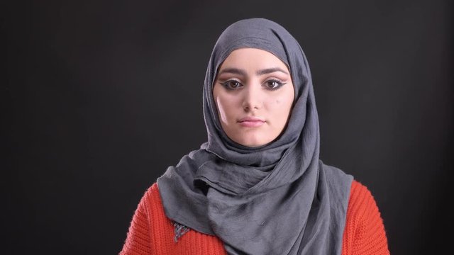 Portrait of beautiful muslim woman in hijab with bright and shiny make-up watching calmly into camera on black background.