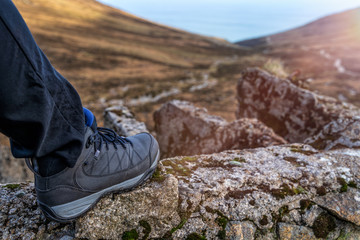 Trekking shoe closeup on a rock in the mountains, valley and sea view during a sunny day, blurred background