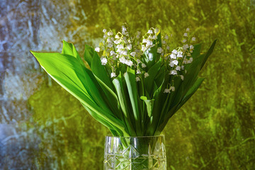 Fototapeta premium A bouquet of lilies of the valley in a glass vase, lilies of the valley on a blue marble background with yellow backlight.