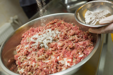 Stuffing with beef in the bowl with stainless steel, the cook prepares the mince for the cocktail, adds a couple of spoons of flour