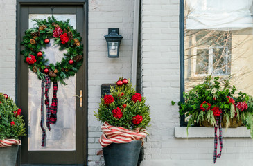 Front door and window of family home decorated for Christmas, holiday season. Winter greenery, ribbons,bulbs and flowers.