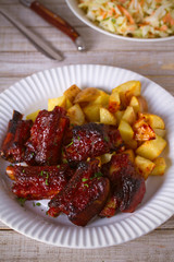 Grilled pork spare ribs with fries on white plate. Roasted sliced barbecue ribs. vertical