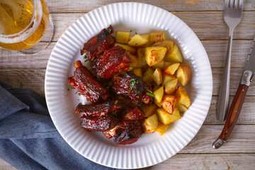 Grilled pork spare ribs with fries on white plate. Roasted sliced barbecue ribs. overhead, horizontal