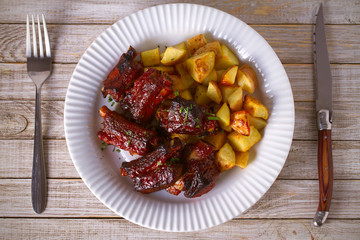 Grilled pork spare ribs with fries on white plate. Roasted sliced barbecue ribs. overhead, horizontal