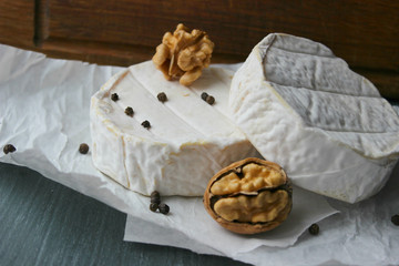 Camembert cheese close-up. Round Camembert cheese on the white paper, the background of the tree. Exquisite cheese, cheese plate, wine food. Camembert cheese. Fresh brie cheese and sliced on a wooden 
