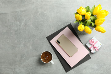 Beautiful tulips in vase and smartphone with accessories on gray background, top view