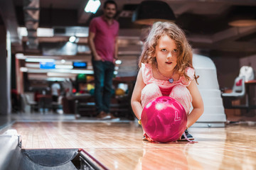 Father and daughter having fun at bowling alley. Proud father watching his little daughter bowling. - obrazy, fototapety, plakaty
