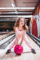 Cute little girl with freckles holding a pink bowling ball, happy with her color choise.