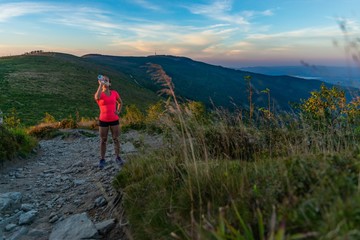 Woman drinking water during running in mountains at summer