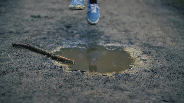 slow motion shot of a woman in blue jeans and dirty old blue vans innocently stepping into a dirty muddy puddle after a rain storm during winter 