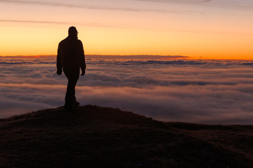 Fototapeta na wymiar Uomo in silhouette al tramonto sopra un mare di nuvole
