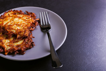 Hash brown and sour cream on a plate on a dark stone background, well fried. Copy space.