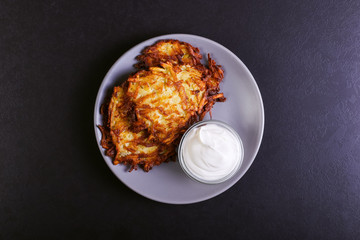 Hash brown and sour cream on a plate on a dark stone background, well fried. Copy space.