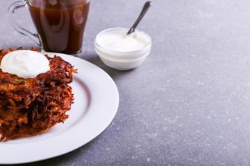 Hash brown and sour cream on a plate against a gray stone background, well fried. Copy space.