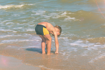 A boy at the sea on the beach washes his hands in the water on the shore.