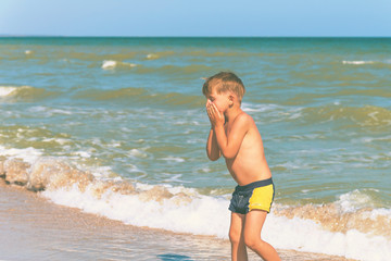 The boy comes out of the water after swimming on the beach in summer on holidays