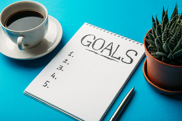 Notepad with Goals List, cup of coffee on blue table, goals concept