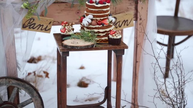 Fruit cake on a stool with wedding rings made of gold during a winter wedding in the middle of a forest on a snow decoration old wooden table on it decorations of coniferous trees