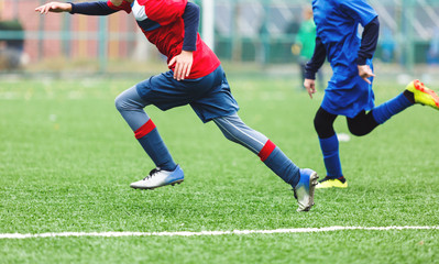 Obraz premium Boys in red white sportswear running on soccer field. Young footballers dribble and kick football ball in game. Training, active lifestyle, sport, children activity concept 