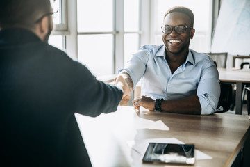 Handshake. Two men of different nationalities, smiling and shaking hands while working in the creative office