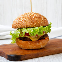 Homemade cheeseburger on rustic wooden board over white wooden background, side view. Closeup.