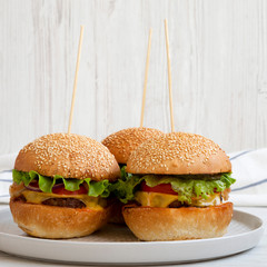 Homemade cheeseburgers on grey plate on white wooden surface, side view. Close-up.