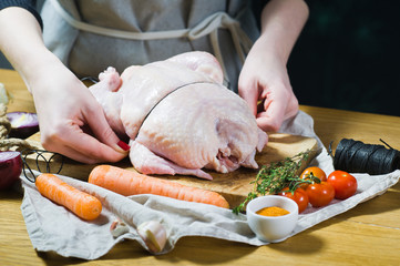Hands of a chef require a piece of raw chicken. Dark background, side view
