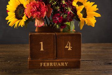 Bouquet of white yellow and red flowers in a clay vase on a dark background for Sant Valentine Day. Vintage wooden Perpetual calendar for Febtuary 14th.
