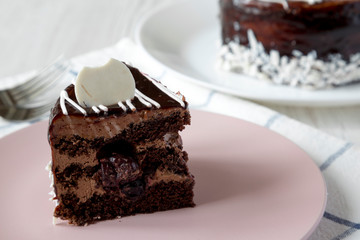 Piece of homemade chocolate cherry cake on a pink plate over white wooden background, side view. Close-up.