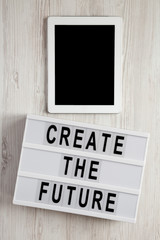 Lightbox with text 'Create the future', tablet on a white wooden background, top view. From above, flat lay, overhead.
