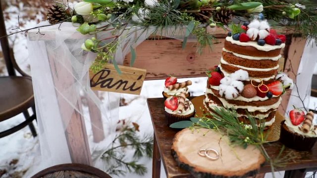 Wedding cake with wedding rings made of gold during a winter wedding in the middle of a forest on a snow decoration old wooden table on it decorations of coniferous trees