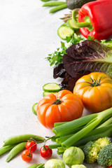 Fresh raw ingredients tomatoes cucumbers lettuce pepper avocado parsley spring onion broccoli peas on the white table, top view, copy space, selective focus