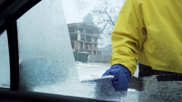 A man removes ice from a side window of a car