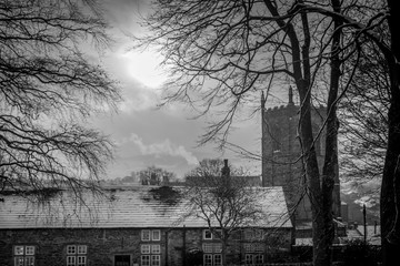church tower or spire with roof tops of houses. snow with a winter sun. black and white. 
