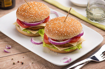 Hamburger with double cheese, red onions and tomatoes on a white rectangular plate on a bright table in the restaurant.
