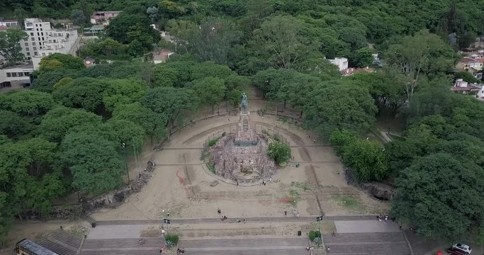 Descending aerial view over monument of General Martin Miguel de Guemes, Salta. Green lush trees surrounding monument.