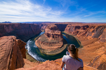 Young woman sitting in the edge of the Horseshoe Bend admiring the landscape. Page, Arizona, United...