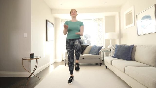 Young blonde woman with edgy pixie cut does knee taps in modern living room